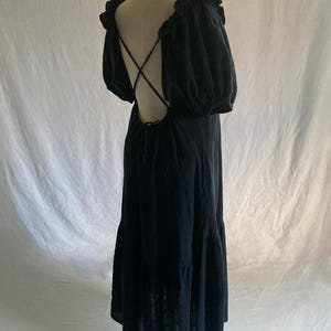 May include: A black maxi dress with a low back and crisscross straps. The dress features ruffled sleeves and a tiered skirt. The dress is displayed on a mannequin against a white backdrop.