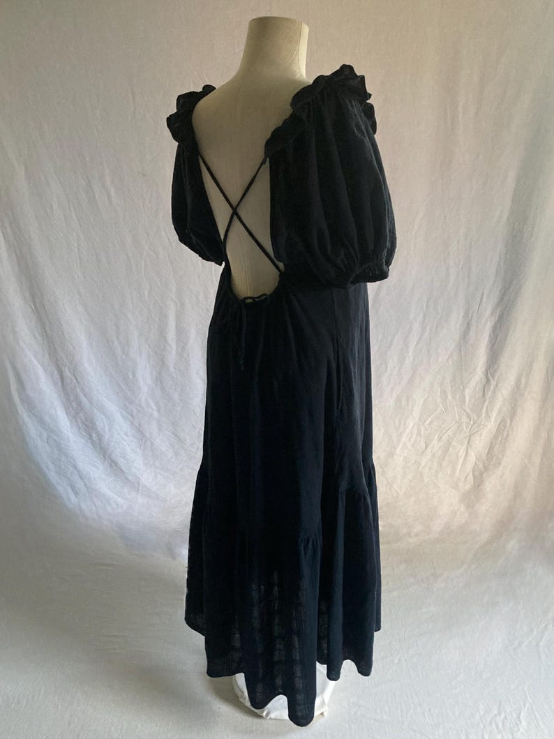 May include: A black maxi dress with a low back and crisscross straps. The dress features ruffled sleeves and a tiered skirt. The dress is displayed on a mannequin against a white backdrop.