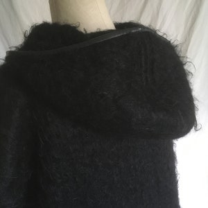 May include: A black fuzzy sweater with a leather strap detail around the neck.