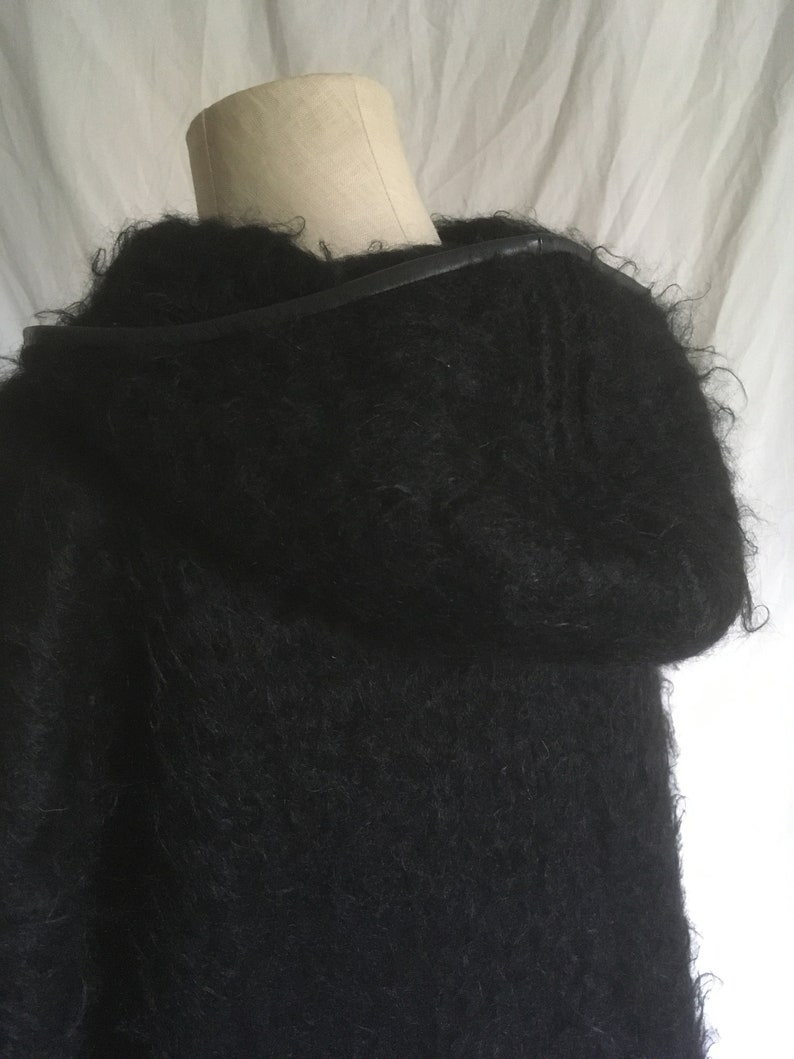 May include: A black fuzzy sweater with a leather strap detail around the neck.