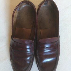 May include: A pair of dark brown leather loafers with a simple design. The loafers have a rounded toe and a single strap across the vamp.