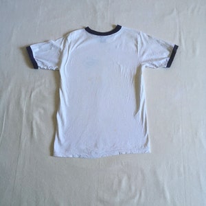 May include: White t-shirt with a black ringer neckline and black ringer sleeves.