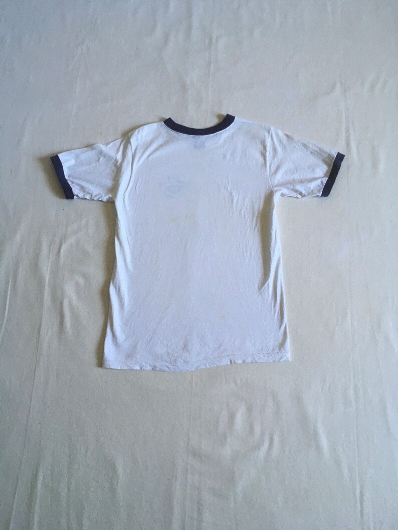 May include: White t-shirt with a black ringer neckline and black ringer sleeves.