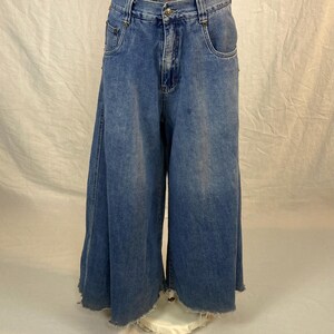 K&ouml;nnte beinhalten: Blaue Jeans-Culottes mit weitem Bein und ausgefranstem Saum. Die Jeans haben ein klassisches F&uuml;nf-Taschen-Design und einen Knopf- und Rei&szlig;verschluss. Die Taille ist hoch. Das Kleidungsst&uuml;ck wird auf einer wei&szlig;en Schaufensterpuppe pr&auml;sentiert.