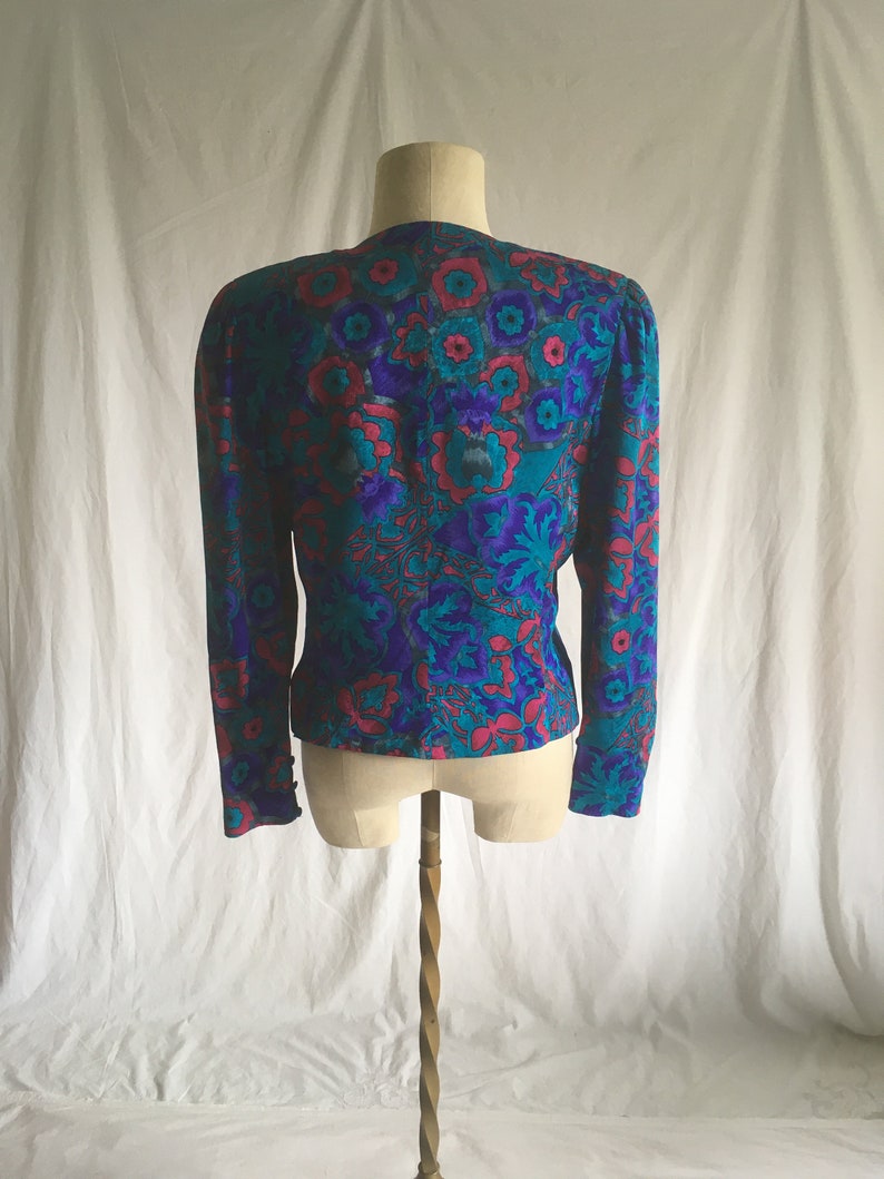 Op de afbeelding: Een blauwe en roze bloemenprint blouse met lange mouwen. De blouse heeft een V-hals en een aansluitende pasvorm.