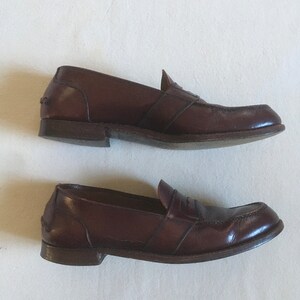 May include: A pair of brown leather loafers with a single strap across the vamp. The loafers have a slightly pointed toe and a low heel.