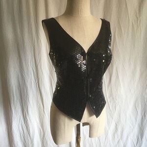 May include: A black sequined vest with a V-neckline and a zipper closure.
