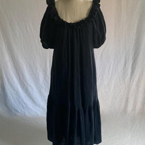 May include: A black dress with a ruffled neckline and short, puffy sleeves. The dress has a flowing, tiered skirt and is displayed on a mannequin against a white backdrop. The dress appears to be made of a soft, lightweight fabric.