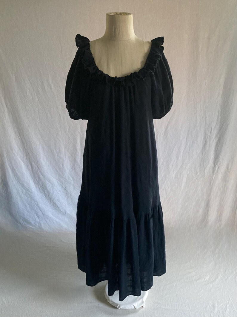 May include: A black dress with a ruffled neckline and short, puffy sleeves. The dress has a flowing, tiered skirt and is displayed on a mannequin against a white backdrop. The dress appears to be made of a soft, lightweight fabric.