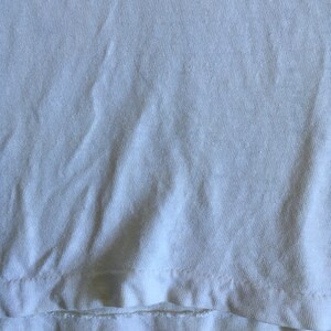 May include: Close-up of a white cotton fabric with a folded edge. The fabric has a slightly textured surface.