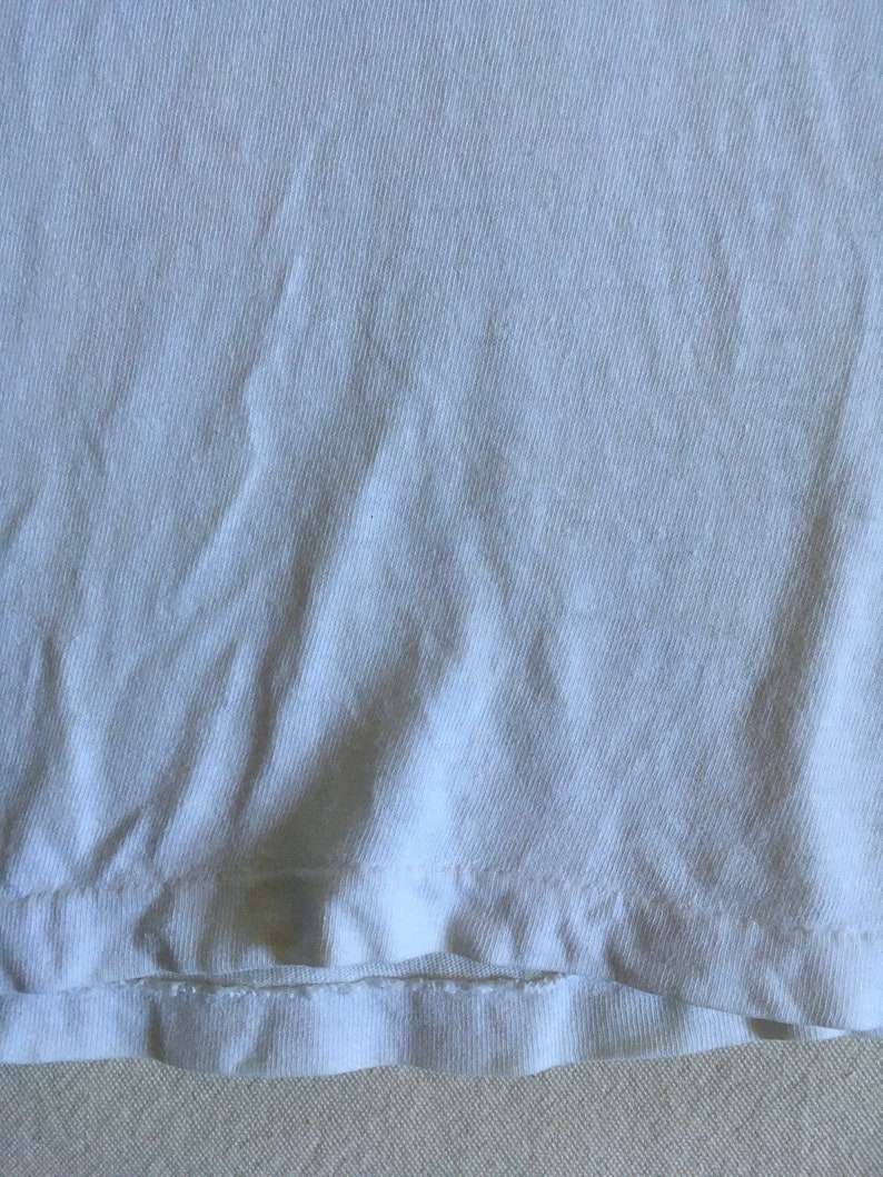 May include: Close-up of a white cotton fabric with a folded edge. The fabric has a slightly textured surface.