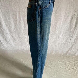 Pu&ograve; includere: Jeans di denim blu chiaro con un classico design a cinque tasche. I jeans hanno un taglio dritto e un lavaggio sbiadito. Una piccola toppa rettangolare &egrave; visibile sulla tasca posteriore. I jeans sono esposti su un manichino.