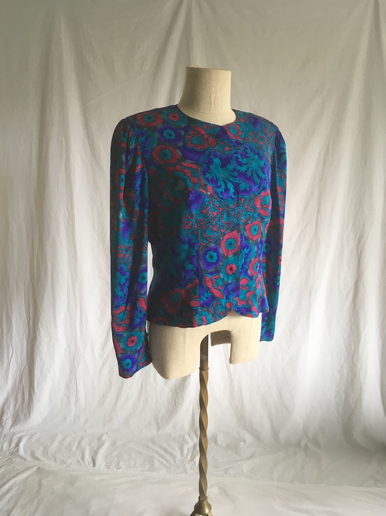 Op de afbeelding: Een blouse met lange mouwen met een levendige bloemenprint in tinten roze, blauw en groen. De blouse heeft een aansluitende pasvorm en een ronde hals.