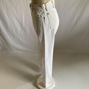 May include: White denim jeans with a classic five-pocket design. The jeans are displayed on a mannequin, showcasing the straight leg cut and the details of the pockets and waistband. The jeans are a bright, solid white.