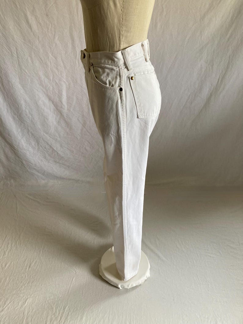 May include: White denim jeans with a classic five-pocket design. The jeans are displayed on a mannequin, showcasing the straight leg cut and the details of the pockets and waistband. The jeans are a bright, solid white.