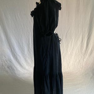May include: A black maxi dress with a ruffled neckline and short, puffed sleeves. The dress features a tiered skirt and a tie-back detail. The fabric appears to be a lightweight material, suitable for warmer weather. The dress is displayed on a mannequin.