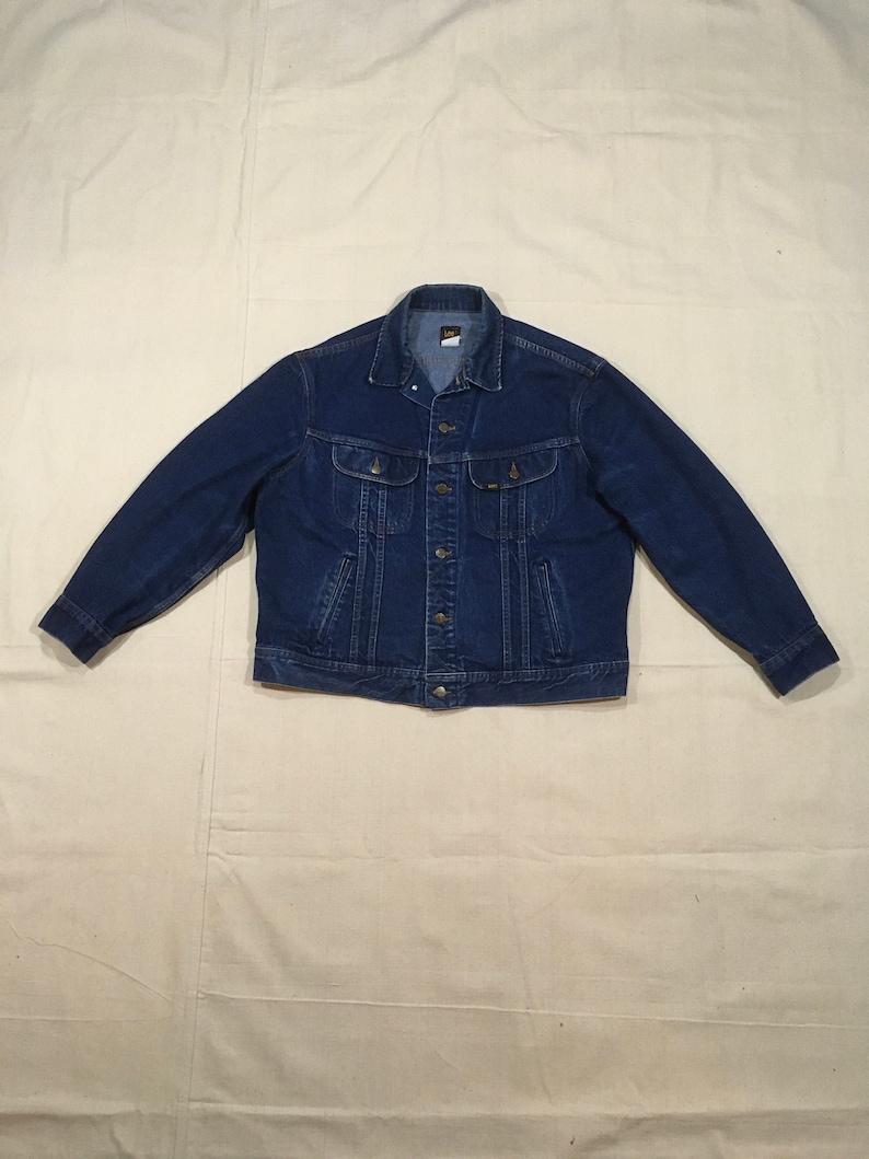 Op de afbeelding: Een donkerblauw denim jack met een knoopsluiting en twee borstzakken. Het jack heeft een merklabel op de linkerzak.
