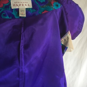 Op de afbeelding: Een paarse zijden jurk met een kraag met bloemenprint. Het label vermeldt "Adrianna Papell" en "100% Zijde" met maat 12 en "Gemaakt in Korea".