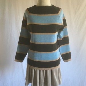 May include: A striped sweater with brown, blue, and beige stripes. The sweater has a round neckline and long sleeves. The sweater is paired with a beige skirt.