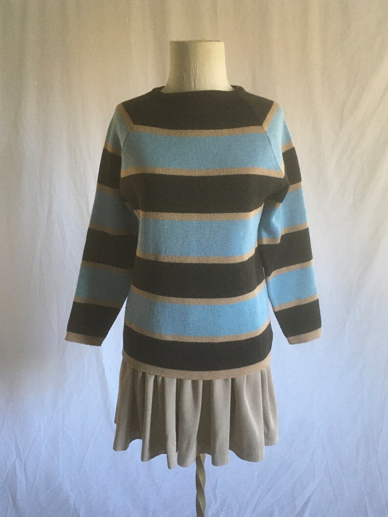 May include: A striped sweater with brown, blue, and beige stripes. The sweater has a round neckline and long sleeves. The sweater is paired with a beige skirt.