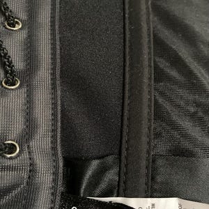 May include: Close-up of a black satin fabric label with white text that reads "frederick's of Hollywood" and "100% Acetate Satin". The label also includes the text "Exclusive of Trimming" and "Made in Canada".