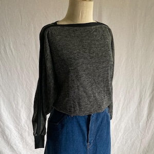 May include: A gray long-sleeved sweater with a square neckline and black trim. The sweater is paired with a blue denim skirt. The sweater has a textured appearance and the sleeves have black cuffs.