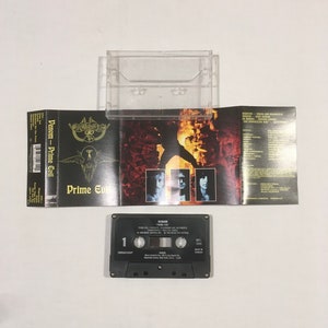 May include: A black cassette tape with the title "Venom - Prime Evil" on the label. The cassette tape is in a clear plastic case with a black and white album cover featuring a figure in a fiery background.