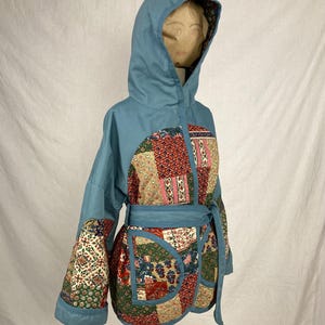 May include: A blue hooded jacket with a patchwork design featuring various floral patterns in shades of red, pink, green, and beige. The jacket has a tie belt and long sleeves.