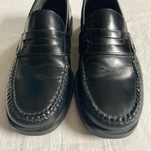 May include: A pair of black leather penny loafers. These classic shoes have a rounded toe, a strap across the vamp, and a stitched sole. The loafers are designed for comfort and style, suitable for various occasions.