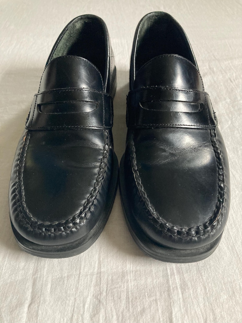 May include: A pair of black leather penny loafers. These classic shoes have a rounded toe, a strap across the vamp, and a stitched sole. The loafers are designed for comfort and style, suitable for various occasions.