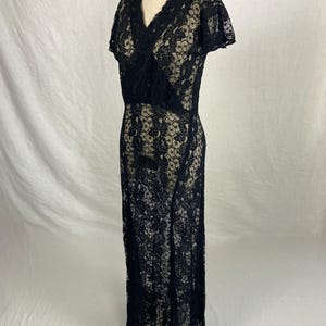 May include: A black lace maxi dress with a V-neckline and short sleeves. The dress has a fitted bodice and a flowing skirt.
