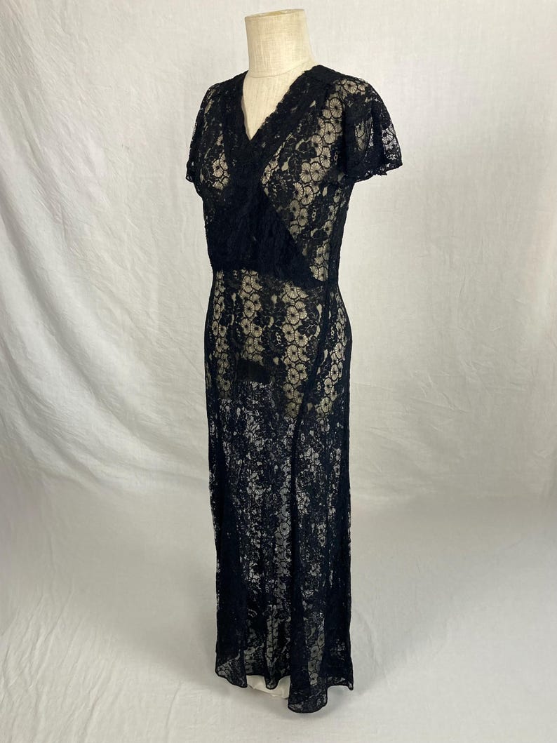 May include: A black lace maxi dress with a V-neckline and short sleeves. The dress has a fitted bodice and a flowing skirt.