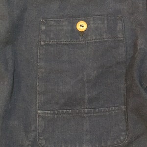 May include: A close-up of a dark blue fabric with a single button on a patch pocket.