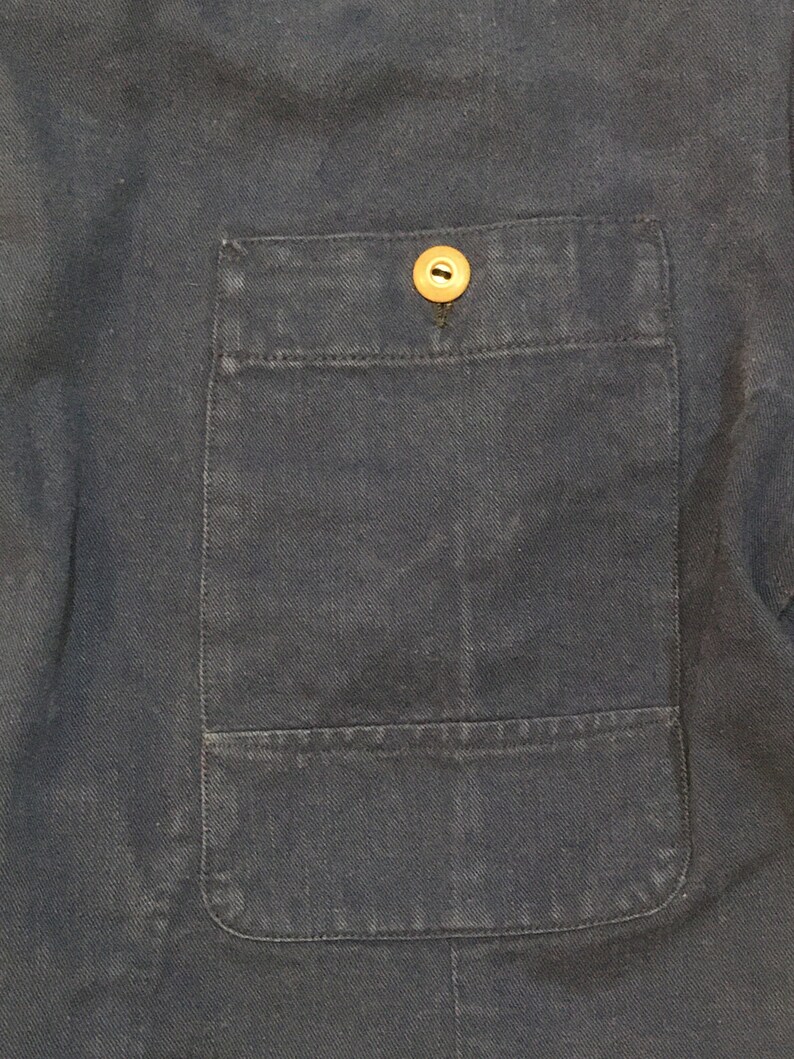 May include: A close-up of a dark blue fabric with a single button on a patch pocket.