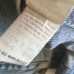 May include: Close-up of a light blue denim jacket with a white care label. The label has text that reads "Machine Wash Cold, Tumble Dry Low, Do Not Bleach, Do Not Iron, Do Not Dry Clean, Made in U.S.A."