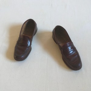 May include: A pair of brown leather loafers with a penny strap detail. The loafers are on a white surface.