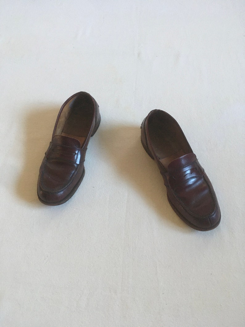 May include: A pair of brown leather loafers with a penny strap detail. The loafers are on a white surface.