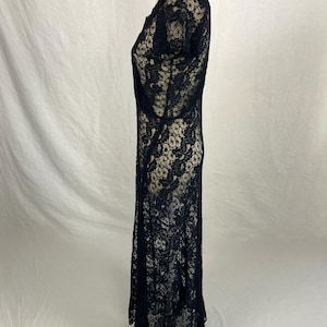 May include: A black lace maxi dress with a scoop neck and short sleeves. The dress is made of a delicate, sheer fabric and has a flowing silhouette.