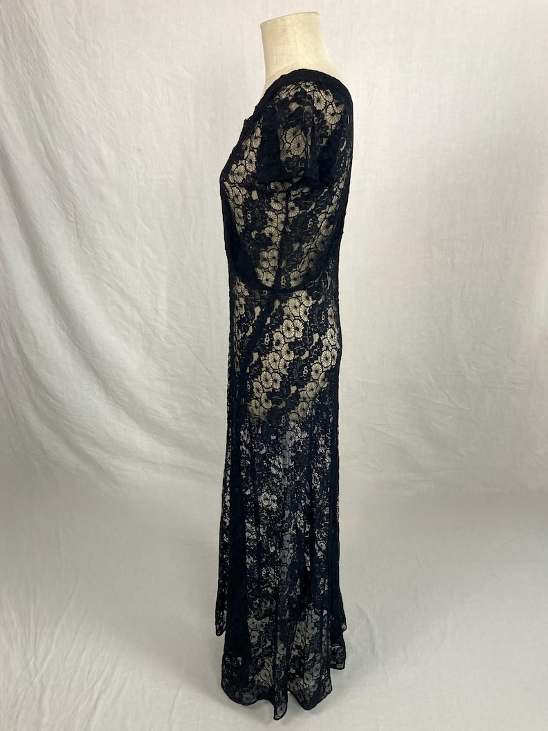 May include: A black lace maxi dress with a scoop neck and short sleeves. The dress is made of a delicate, sheer fabric and has a flowing silhouette.