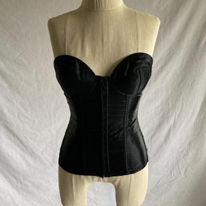 May include: A black satin strapless corset with boning and a lace-up front.