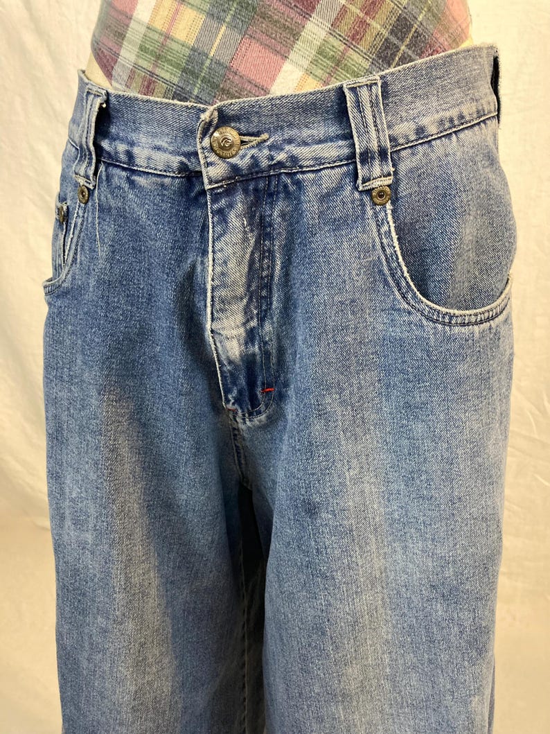 K&ouml;nnte beinhalten: Hellblaue Jeans mit Knopfverschluss und Vordertaschen. Die Jeans haben eine verwaschene Waschung und ein klassisches F&uuml;nf-Taschen-Design. Die Jeans sind im Vintage-Stil.