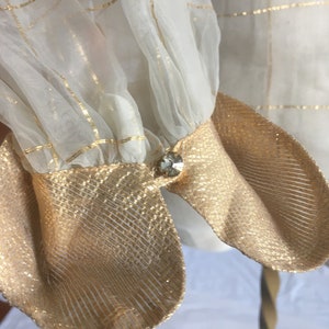 May include: White sheer blouse with gold thread detailing and gold fabric cuffs. The cuffs have a small clear rhinestone button.