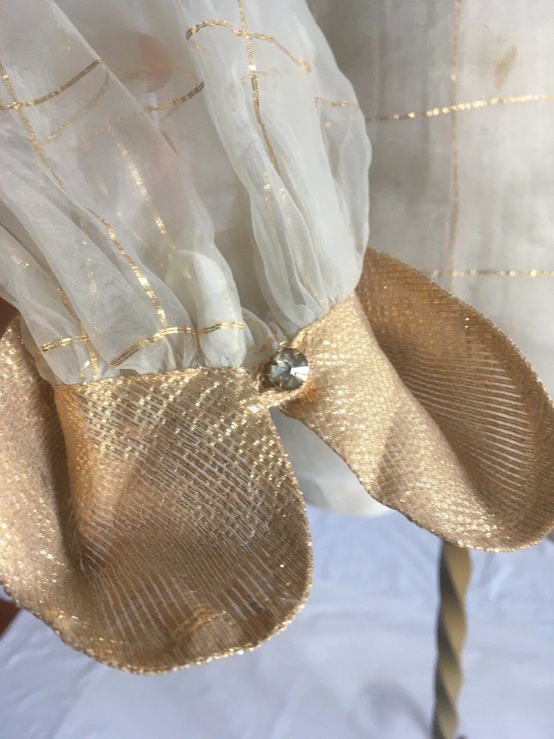 May include: White sheer blouse with gold thread detailing and gold fabric cuffs. The cuffs have a small clear rhinestone button.