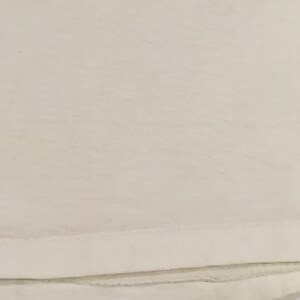 Op de afbeelding: Een wit T-shirt met een effen ontwerp. Het shirt heeft een dubbel gestikte zoom.