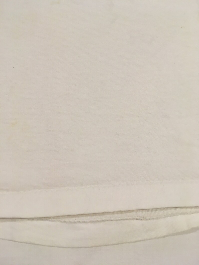 Op de afbeelding: Een wit T-shirt met een effen ontwerp. Het shirt heeft een dubbel gestikte zoom.