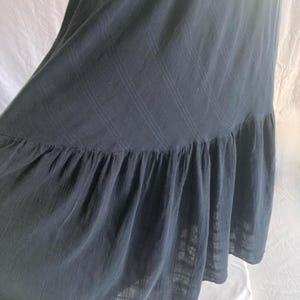 May include: A dark gray maxi dress with a ruffled hem. The dress is made of a lightweight fabric and has a subtle plaid pattern. The fabric drapes loosely, creating a flowing silhouette.