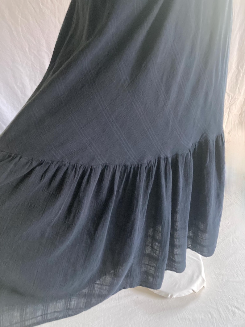 May include: A dark gray maxi dress with a ruffled hem. The dress is made of a lightweight fabric and has a subtle plaid pattern. The fabric drapes loosely, creating a flowing silhouette.