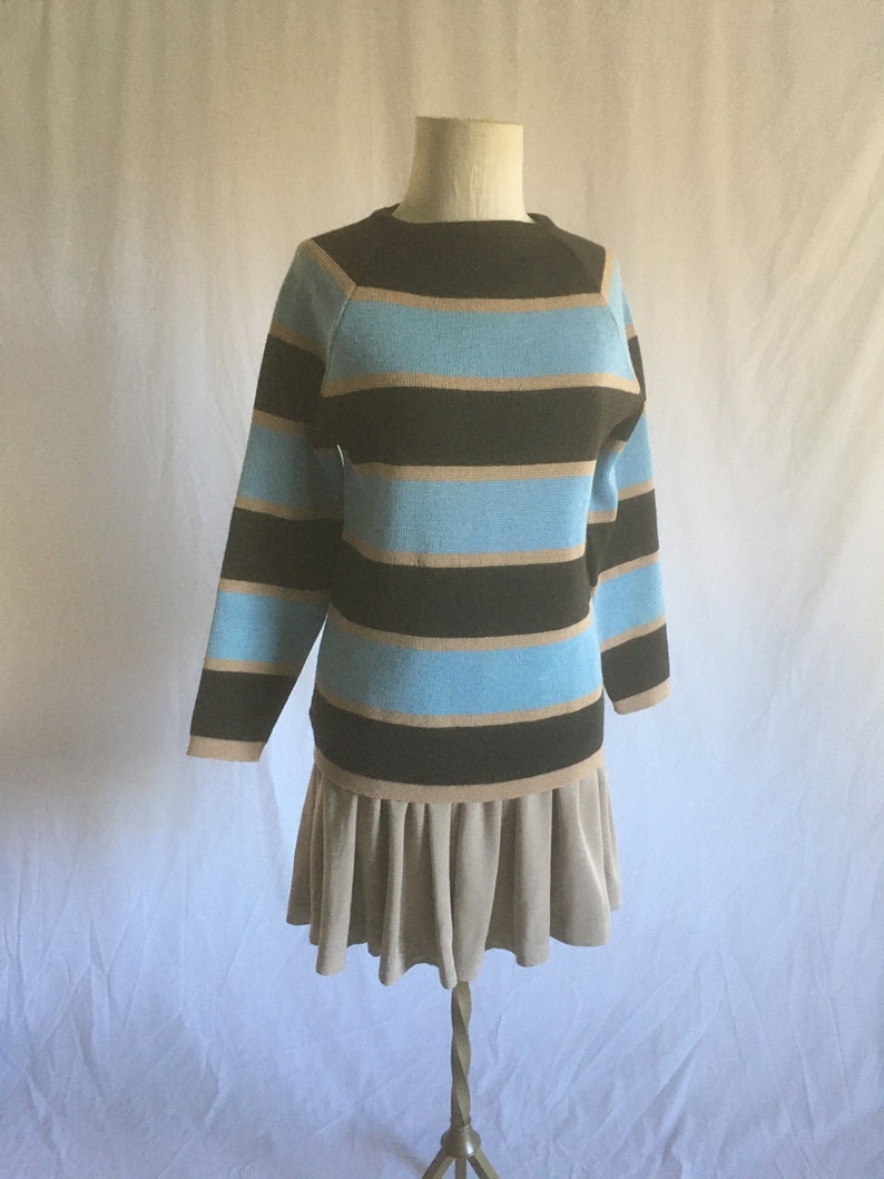 May include: A striped sweater dress with brown and blue horizontal stripes. The dress has a brown collar and a beige skirt with pleats.