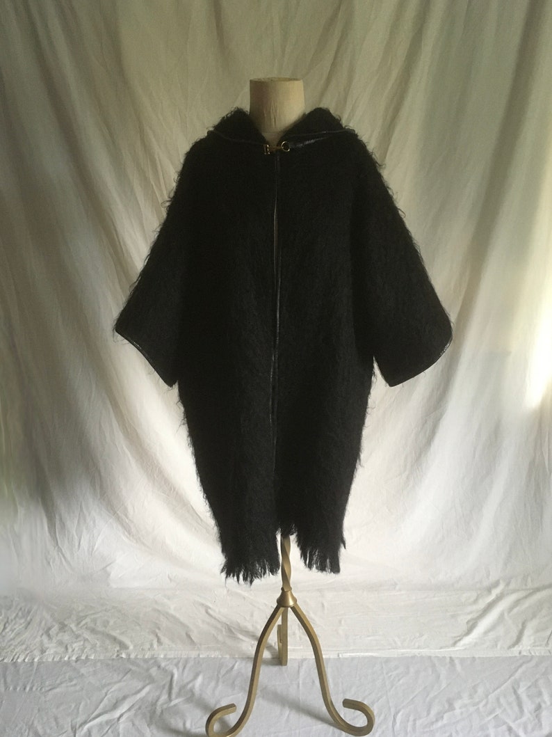 May include: Black hooded sweater with a zipper closure and fringe detailing. The sweater is made of a soft, fuzzy material.