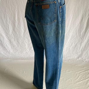 Pu&ograve; includere: Jeans in denim blu dalla vestibilit&agrave; classica. Presentano una toppa in pelle marrone sulla tasca posteriore con il marchio Wrangler e rivetti color rame. I jeans hanno un lavaggio sbiadito e una gamba dritta.
